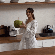 a woman holding a coconut in a kitchen with a smeg coffee maker in the background