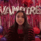 a woman is sitting in front of a wall with balloons and tinsel .