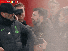 a man wearing a jacket that says ' axa ' on it talks to another man