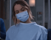 a woman wearing a surgical mask and a gown is sitting in a chair .