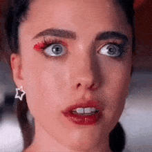 a close up of a woman 's face with a star earring and red eye shadow .