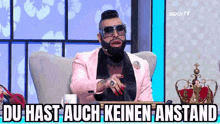 a man with a beard and sunglasses is sitting in a chair and talking into a microphone .