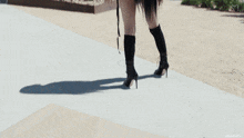 a woman in knee high boots is walking down a sidewalk .