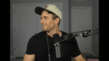 a man wearing a hat and headphones stands in front of a black microphone