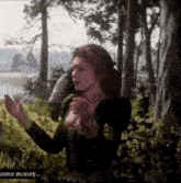 a woman is standing in the woods holding a bird in her hands .