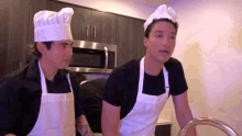 two men wearing chef hats and aprons are standing in a kitchen