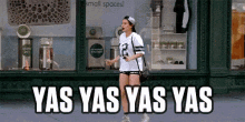 a woman is walking down the street with the words yas yas yas yas in front of a store .