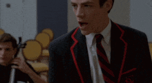 a man in a suit and tie stands in front of a man playing cello