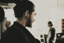 a man with a beard and a bun is standing in a room with other people .