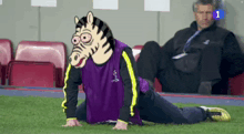 a man wearing a zebra mask is stretching on the grass