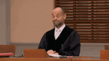 a man in a judge 's robe sits at a desk in front of a laptop