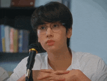 a man wearing glasses is sitting in front of a microphone .