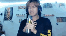 a man wearing headphones holds a bottle in front of his chest and has the letter b on his arm