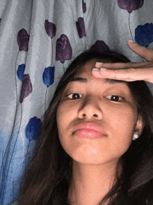 a girl with a ring on her finger touches her forehead in front of a curtain with purple and blue flowers