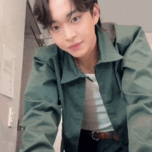 a young man wearing a green jacket and a necklace is looking at the camera