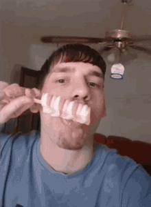 a man in a blue shirt is brushing his teeth while a ceiling fan hangs from the ceiling
