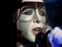 a woman with a mask on her face is singing into a microphone in a dark room .