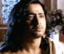 a man with long hair is standing in front of a window .