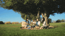 three women are having a picnic under a tree one of them is playing a guitar