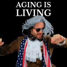 a man in a wig and scarf is dancing in front of a sign that says aging is living