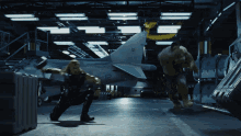 hulk and thor are fighting in a hangar with a plane in the background with the number 12 on it