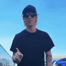 a man wearing sunglasses , a hat and a black shirt is giving the middle finger .