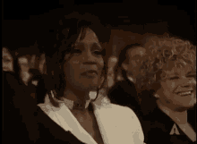 a woman wearing a choker and a white jacket is sitting in a crowd .
