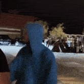 a person wearing a blue hoodie is standing in a parking lot at night