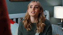 a woman is sitting on a bed wearing a grey sweater and a necklace .