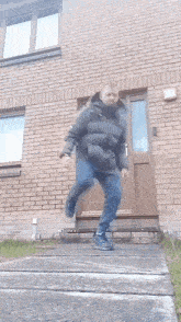 a man in a black jacket is jumping in front of a brick building .