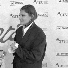 a woman in a suit is standing in front of a wall that says gts music
