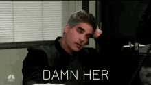a man is sitting at a desk with his hand on his head and the words " damn her " written above him