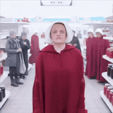 a woman in a red cape and white hat stands in a grocery store surrounded by other women