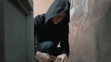 a man in a black hoodie is kneeling down behind a plastic bag