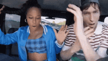 a woman in a blue jacket and a man in a striped shirt are dancing in the back seat of a car