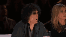 a man with curly hair is sitting in front of a microphone while a woman watches .