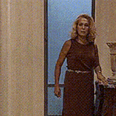a woman in a brown dress is standing in a room next to a vase .