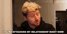 a man with blonde hair and a beard is standing in a room and talking .