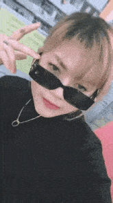 a woman wearing sunglasses and a black turtleneck is making a peace sign .