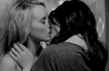 a black and white photo of two women kissing .