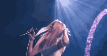 a woman singing into a microphone with a purple light behind her