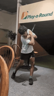 a man is swinging a golf club in front of a sign that says play-a-round
