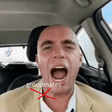 a man in a car with his mouth open and the word groupmates crossed out in red