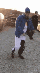 a man in a blue jacket and white pants is dancing in a parking lot
