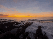 a sunset over a rocky beach with waves crashing on the rocks
