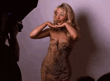 a woman in a gold dress is posing for a picture while a man holds a camera .