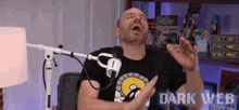 a man is laughing in front of a microphone while wearing a black shirt that says dark web