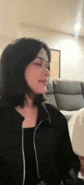 a woman in a black jacket is sitting on a couch in a living room with her eyes closed .