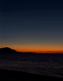 sunset over the ocean with mountains in the background