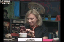 a woman sitting at a table with a cup of coffee and a phone with the word lowstorm on the screen